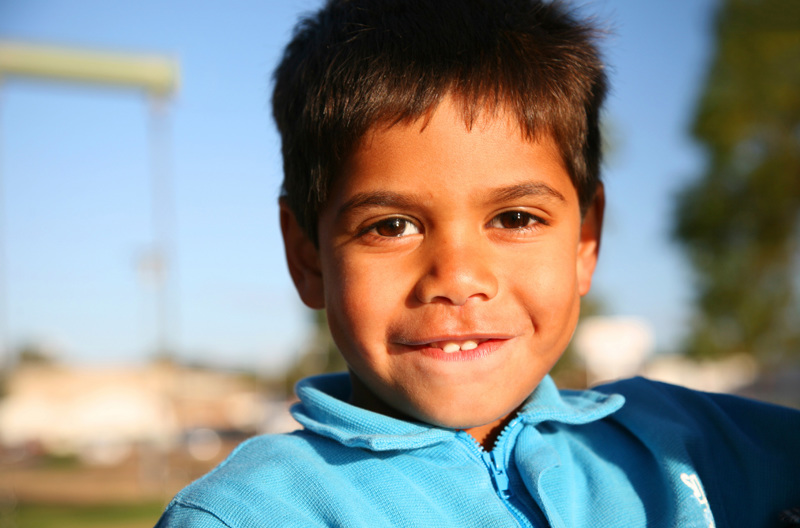 A young boy wearing a light blue shirt standing outside.