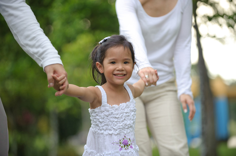 Two parents holding both of their daughters hands.