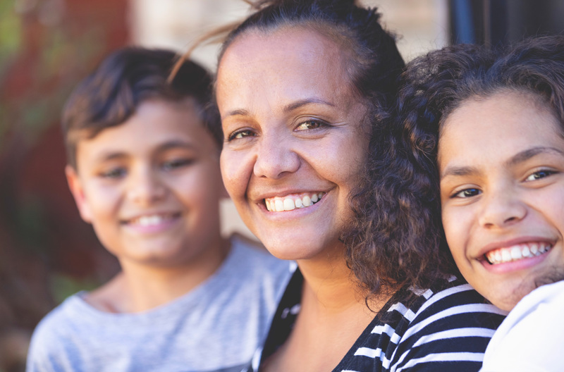 A parent smiling with her two children on either side of her. 