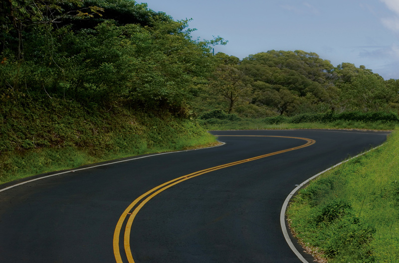 A road winding around a bend through green trees.