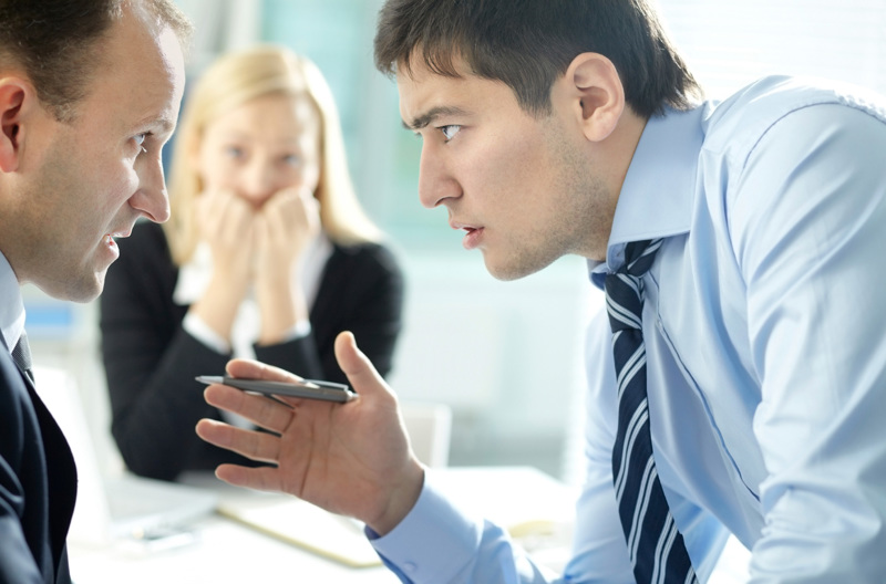 Two people have an intense discussion while another person looks on worriedly in the background.