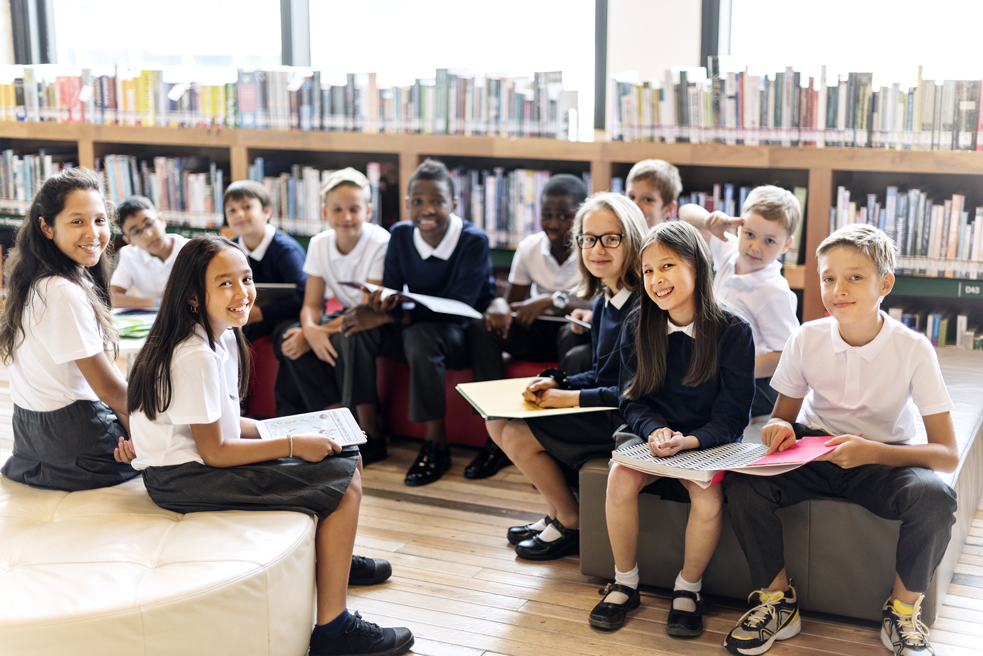 A group of school students sitting down on chairs in a library.