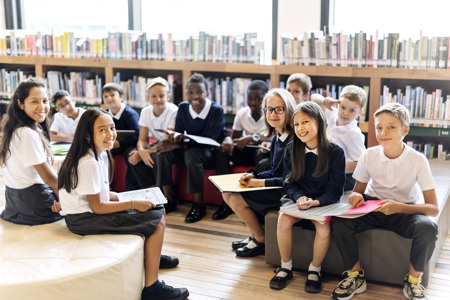 A group of school students sitting down on chairs in a library.