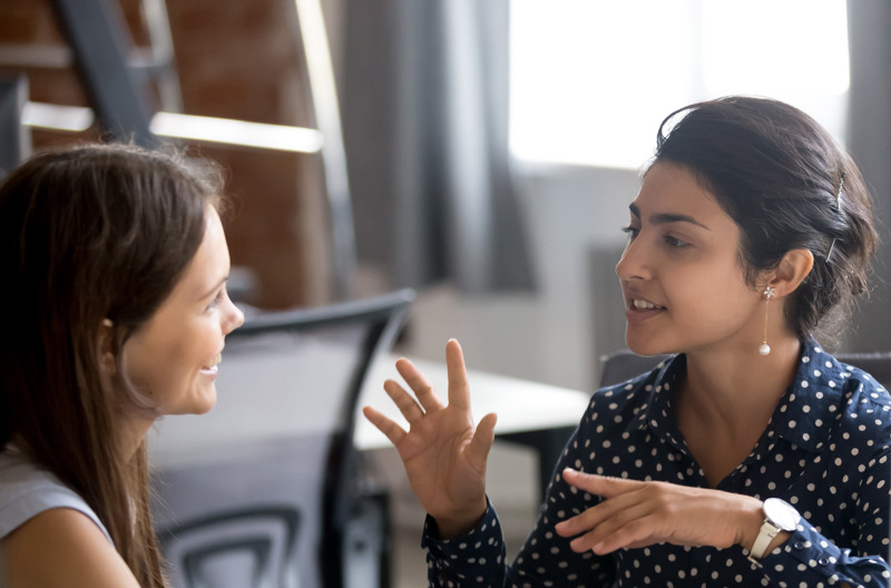 Two female professionals of South Asian and Anglo Saxon heritage having a friendly conversation in the office