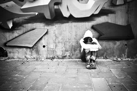 A woman sitting down leaning against a brick wall hugging her knees.