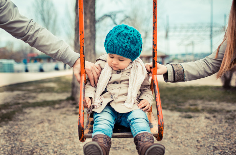 A child on a swing pushed by their parents.