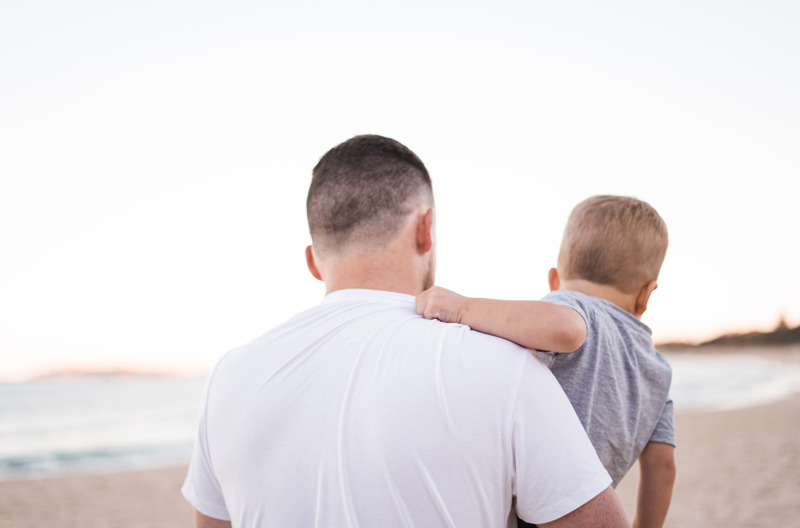 A man standing on a beach holding his infant child. 