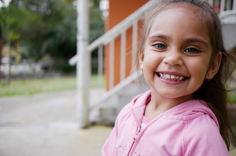 A young girl wearing a pink hoodie standing in front of some stairs outside.