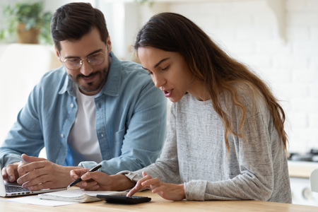 A couple sitting together at a table with a laptop and a calculator in front of them.