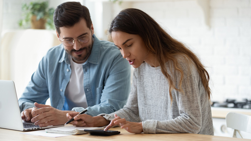 A couple sitting together at a table with a laptop and a calculator in front of them.