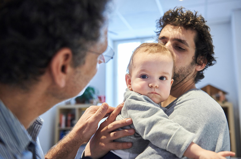 A parent holding his child while a grandparent looks on. 