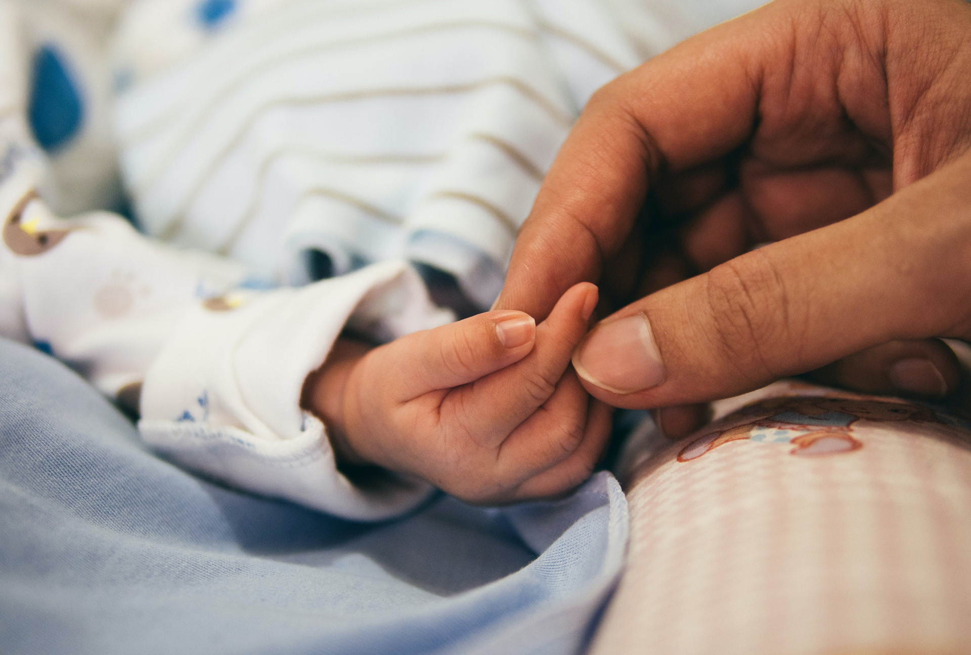 A parent holding their infant baby's fingers. 