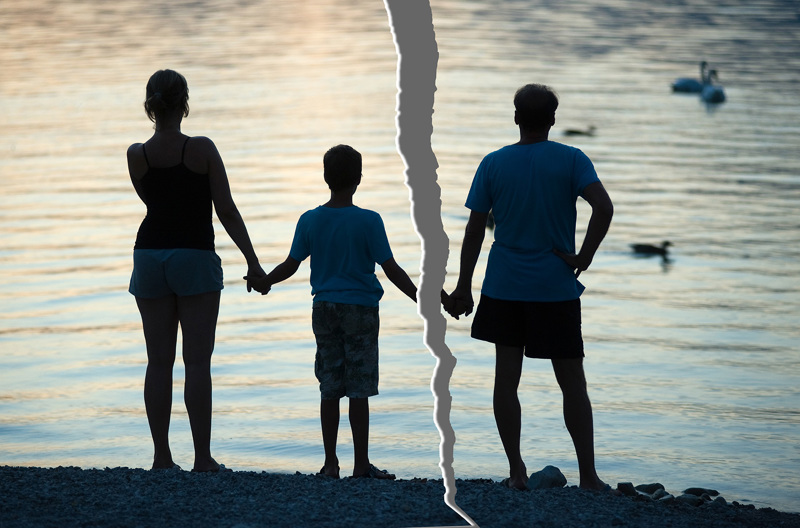 A torn photo of two parents holding their child's hands in front of water.