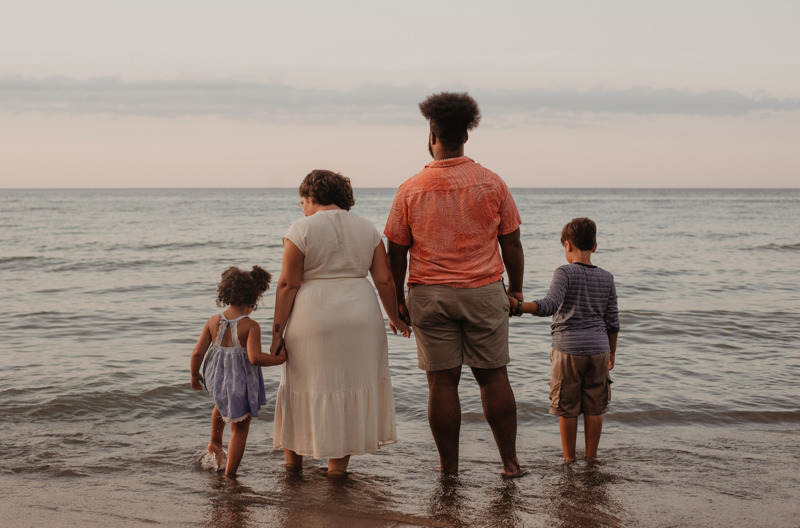 A family standing together at the beach holding hands. 