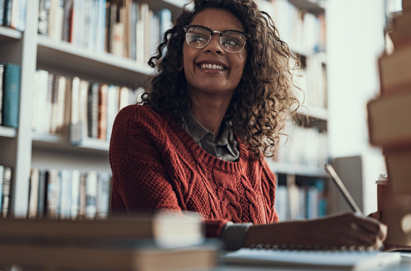 A woman sitting at a desk smiling while taking notes. 