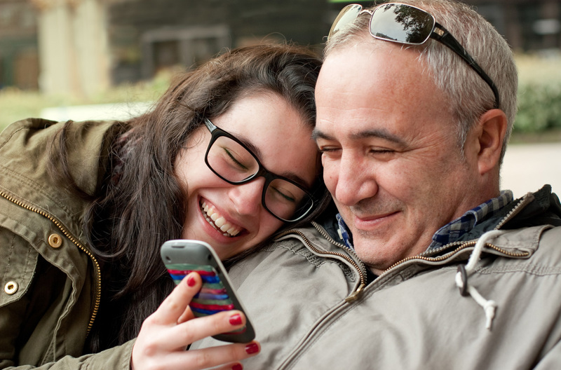 A smiling child showing her parent something on her phone.