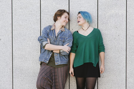 A couple with their backs against a wall, looking at each other.