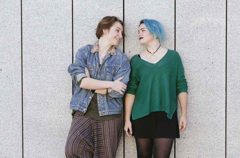 A couple with their backs against a wall, looking at each other.