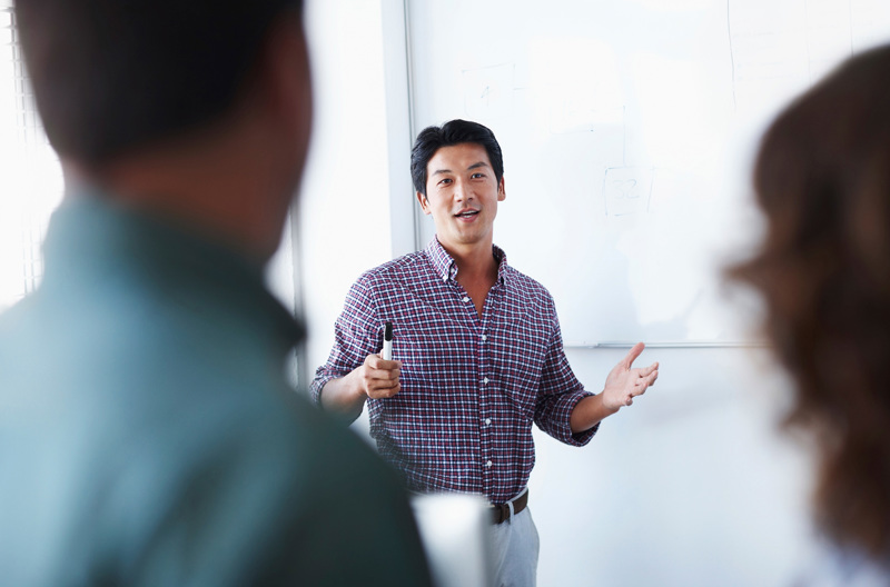 A teacher standing in front of a class holding a whiteboard marker