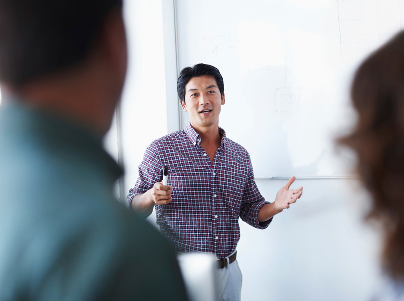 A teacher standing in front of a class holding a whiteboard marker