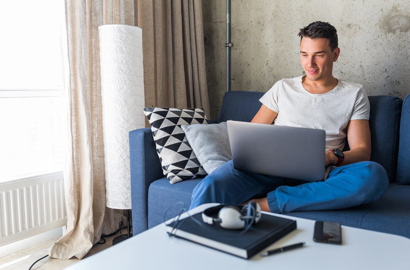 A man sitting down on a blue couch with an open laptop on his lap.