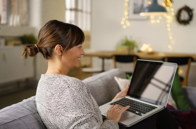 A woman sitting on a couch with an open laptop on her lap.