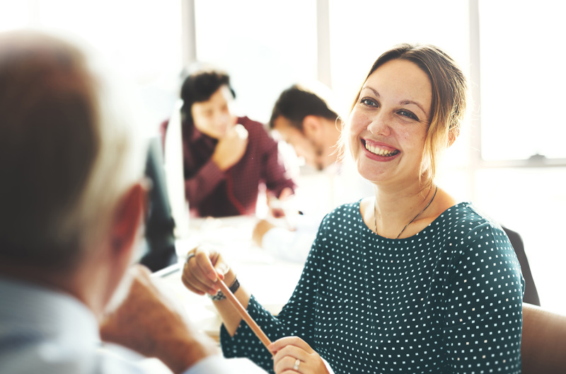 A person holding a pencil smiling while listening to someone else speaking. 