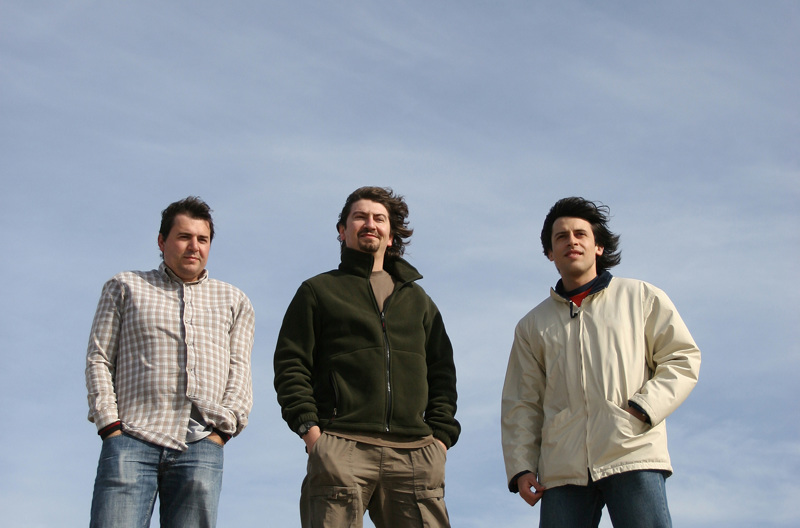 Three people standing together on pebbles at the beach. 