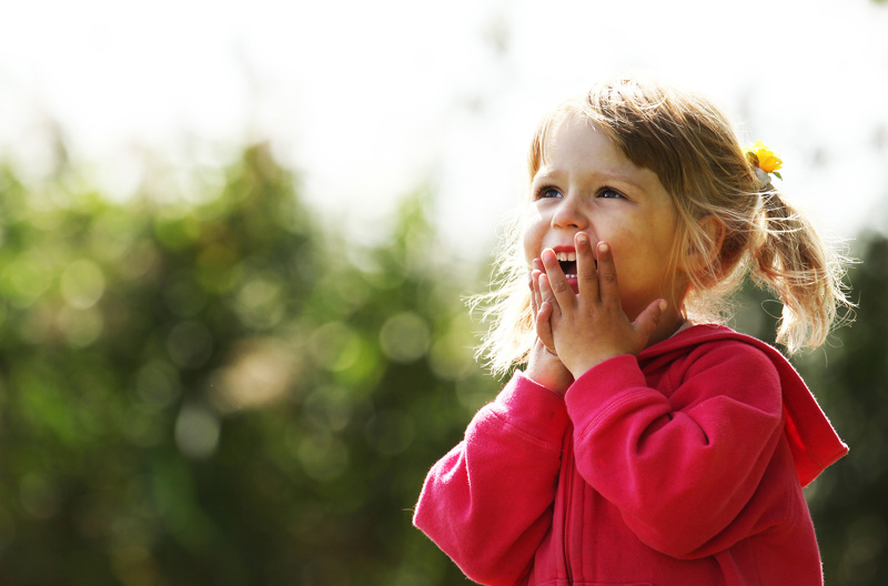 A young girl wearing a pink zip up hoodie covering her mouth with her hands.