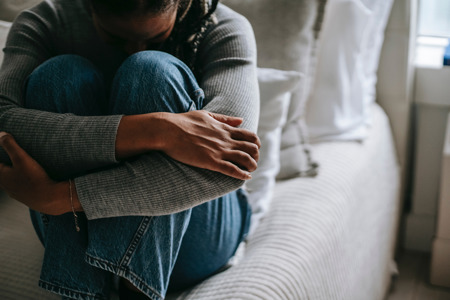 A person sitting on a bed hugging their knees.