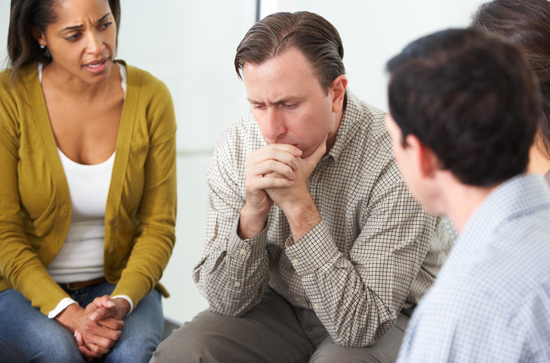 An unhappy man being consoled by a group of people. 