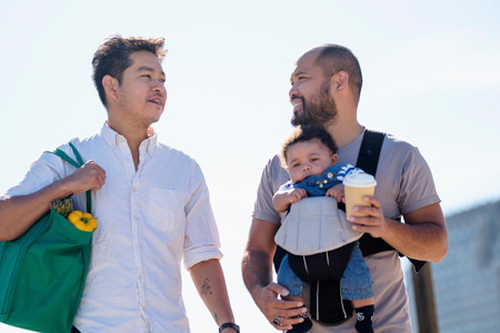 A couple holding their child in a baby carrier.