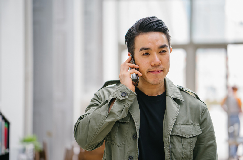 A man wearing a green shirt smiling while on the phone.