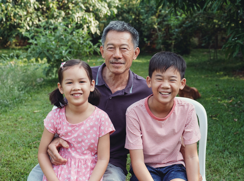 A man sitting outside in a yard with two children