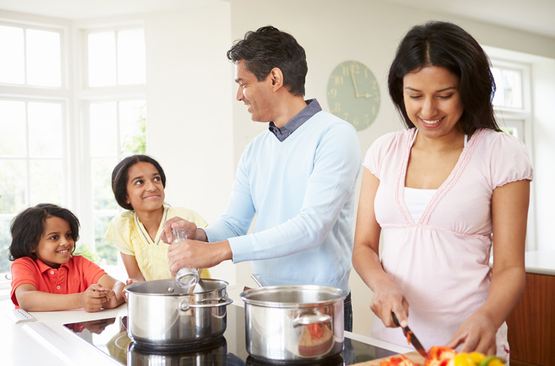 Two parents cooking while their children sit at the end of the bench. 