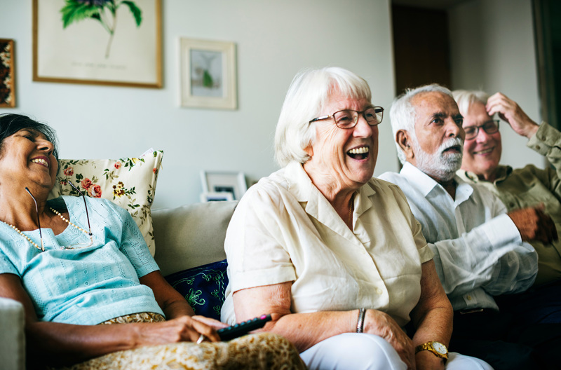 Four people sitting together on a couch laughing. 