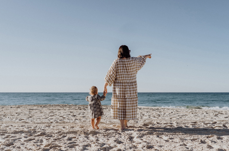 A mother pointing off into the distance while holding her child's hand on the beach. 