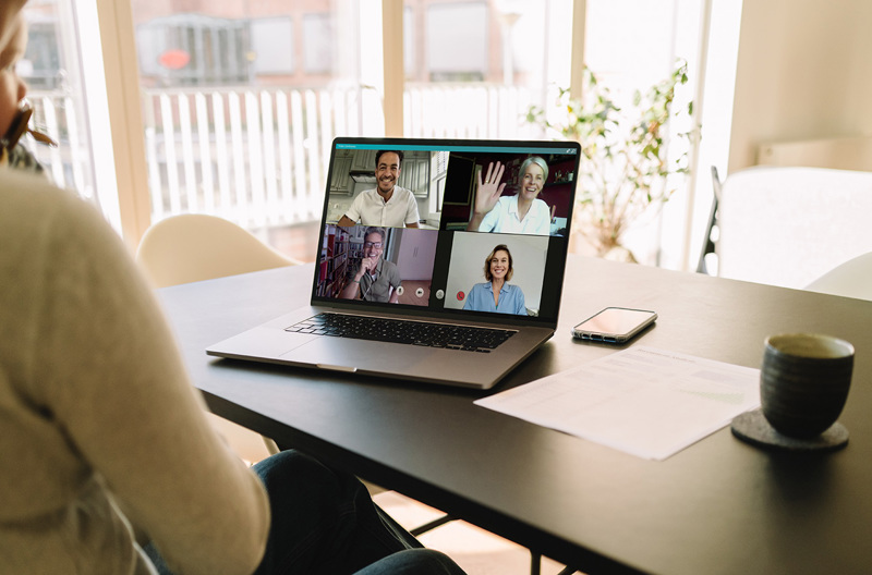 A person sitting at a table with their laptop open on a group video call.