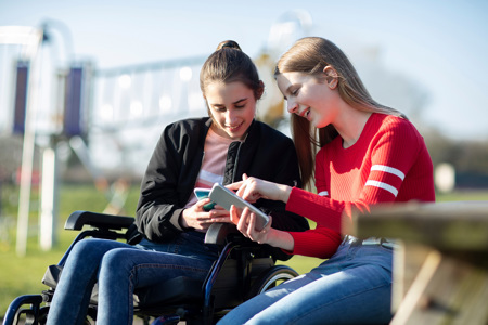 A couple sitting together on a park bench, looking at each others phones.